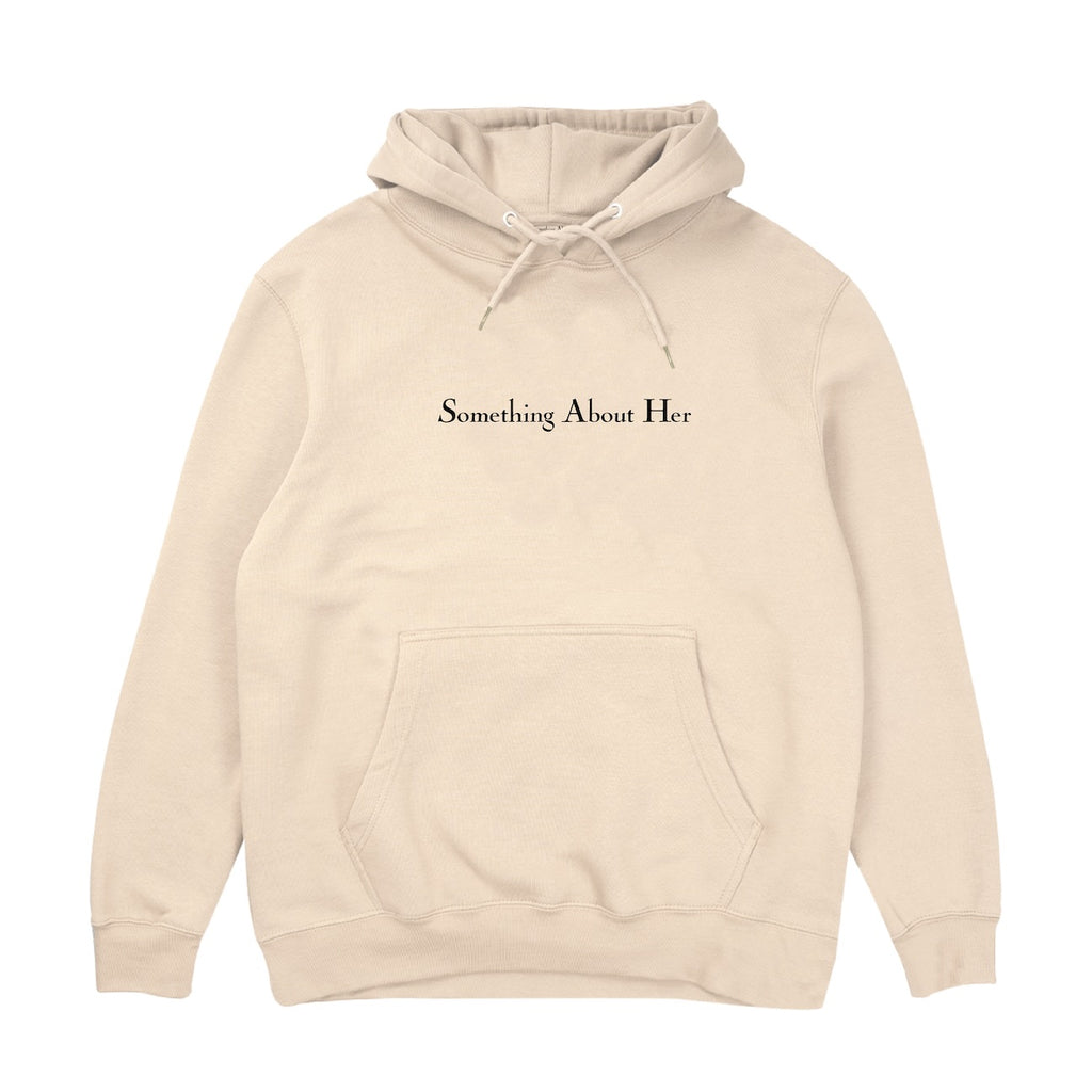 A beige hooded sweatshirt with "Something About Her" embroidered across the chest in black