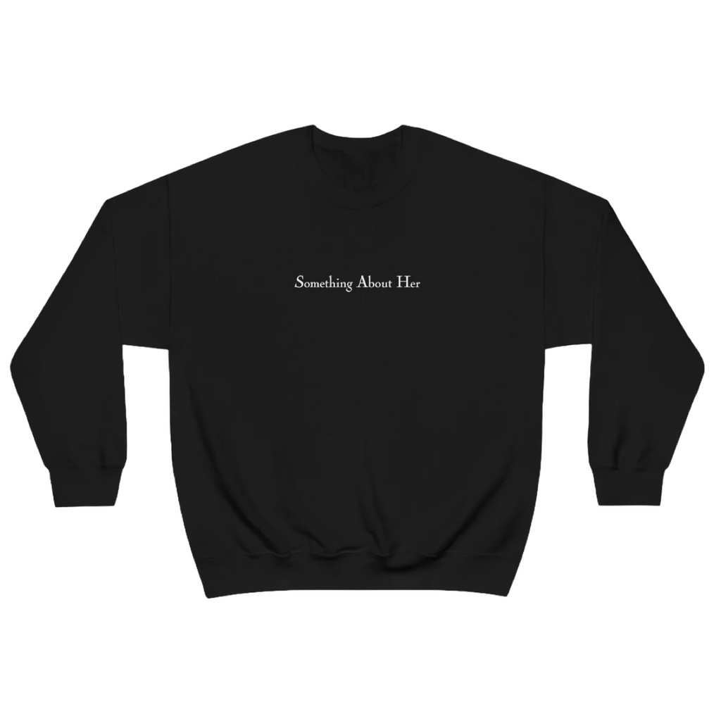 A black crewneck sweatshirt with "Something About Her" embroidered across the chest in white