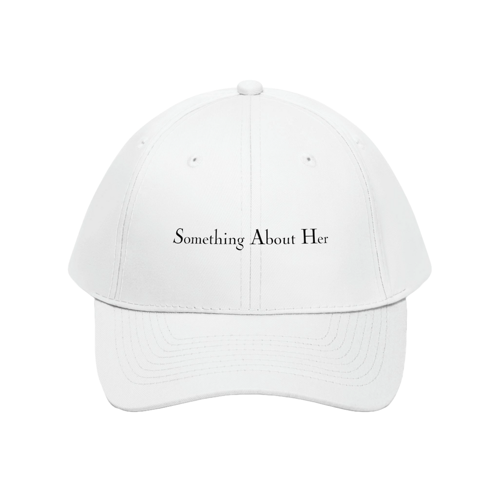 A white dad hat style cap with "Something About Her" embroidered in the middle in black