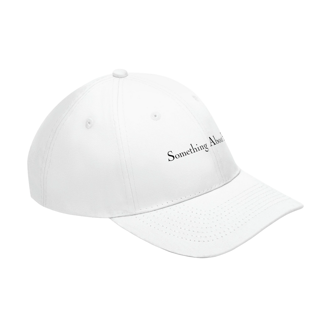 A side view of a white dad hat style cap with "Something About Her" embroidered in the middle in black