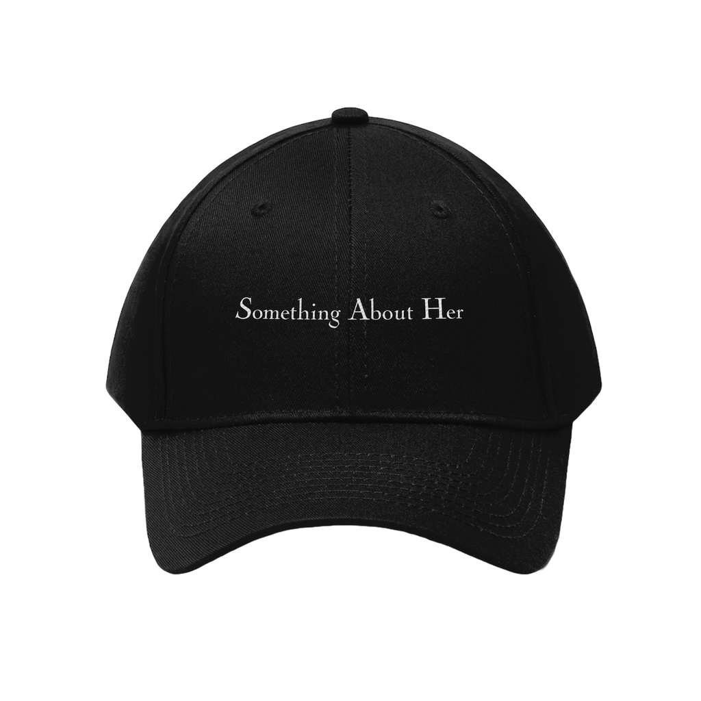 A black dad hat style cap with "Something About Her" embroidered in the middle in white